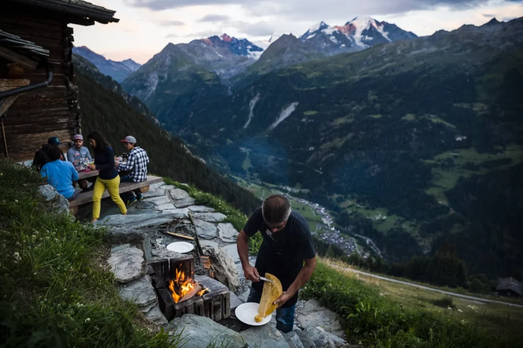 Exclusive to our groups, we enjoy local raclette cooked over an open fire at the Pellissier’s mountain retreat. Way down below over Jean-Marc’s left shoulder is the village of Lourtier and the hotel. Photo: Mattias Fredriksson
